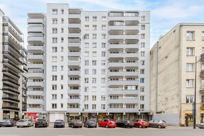 A multi-story residential building with balconies, a ground-level shop, and parked cars. - City Apartment in Warsaw (Warszawa 2)