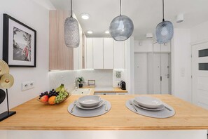 A modern kitchen with a wooden countertop, hanging pendant lights, and a fruit bowl. - Modern Coastal Home with Scenic Terrace Views (Warszawa)
