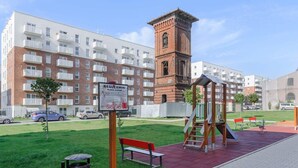 Een speeltuin met een schommel, een bankje, een bakstenen toren en een bordje in een woonwijk.