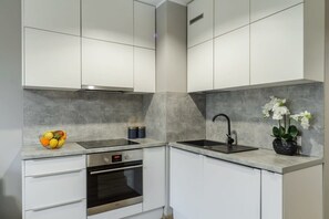 A modern kitchen with white cabinets, a stainless steel oven, a black sink, and a fruit bowl. - Aesthetic Family Stay in Łódź City (Łódź)