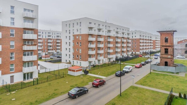 Een meerlaags woongebouw met balkons, een parkeerplaats en een klein bakstenen gebouw.