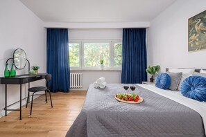Ein Schlafzimmer mit Bett, Schreibtisch, Stuhl, einem Fenster mit Vorhängen und einem Bild an der Wand.