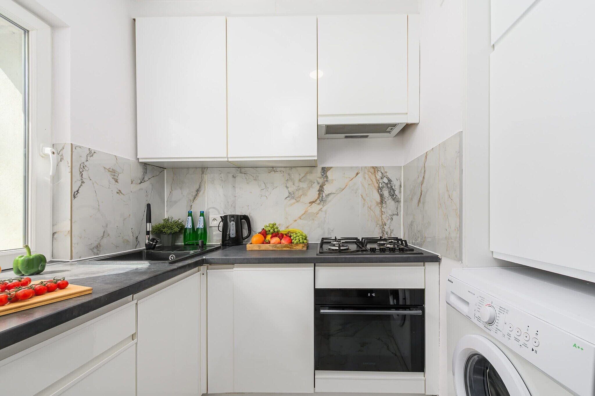 A modern kitchen with white cabinets, a gas stove, a built-in oven, and a washing machine.