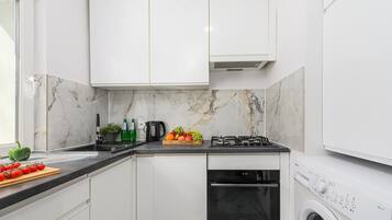 A modern kitchen with white cabinets, a gas stove, a built-in oven, and a washing machine.