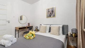 A neatly arranged bedroom with a bed, bedside table, lamp, and a framed artwork on the wall.