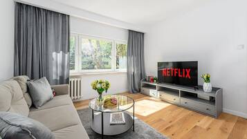 Uma sala de estar moderna com um sofá, uma mesa de centro, uma TV exibindo o logotipo da Netflix e uma janela com cortinas.