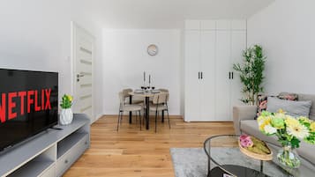 A modern living room with a flat-screen TV, a dining area with a table and chairs, and a sofa with a floral arrangement.