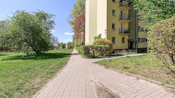A paved pathway leading to a yellow building with multiple balconies, surrounded by greenery and trees.