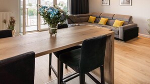 Een moderne woonkamer met een zithoek, een eettafel met stoelen, en een bloevas.
