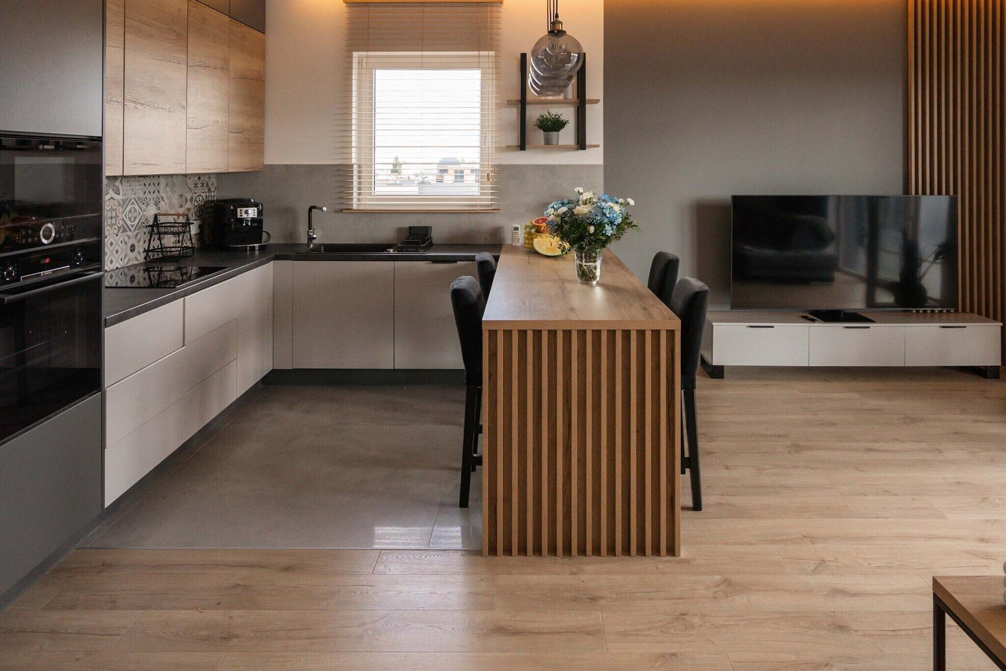 Una cocina moderna con una isla central, horno empotrado y comedor con sillas.