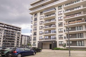 En flereetagers boligbygning med altaner, parkeringsplads og en klar himmel.