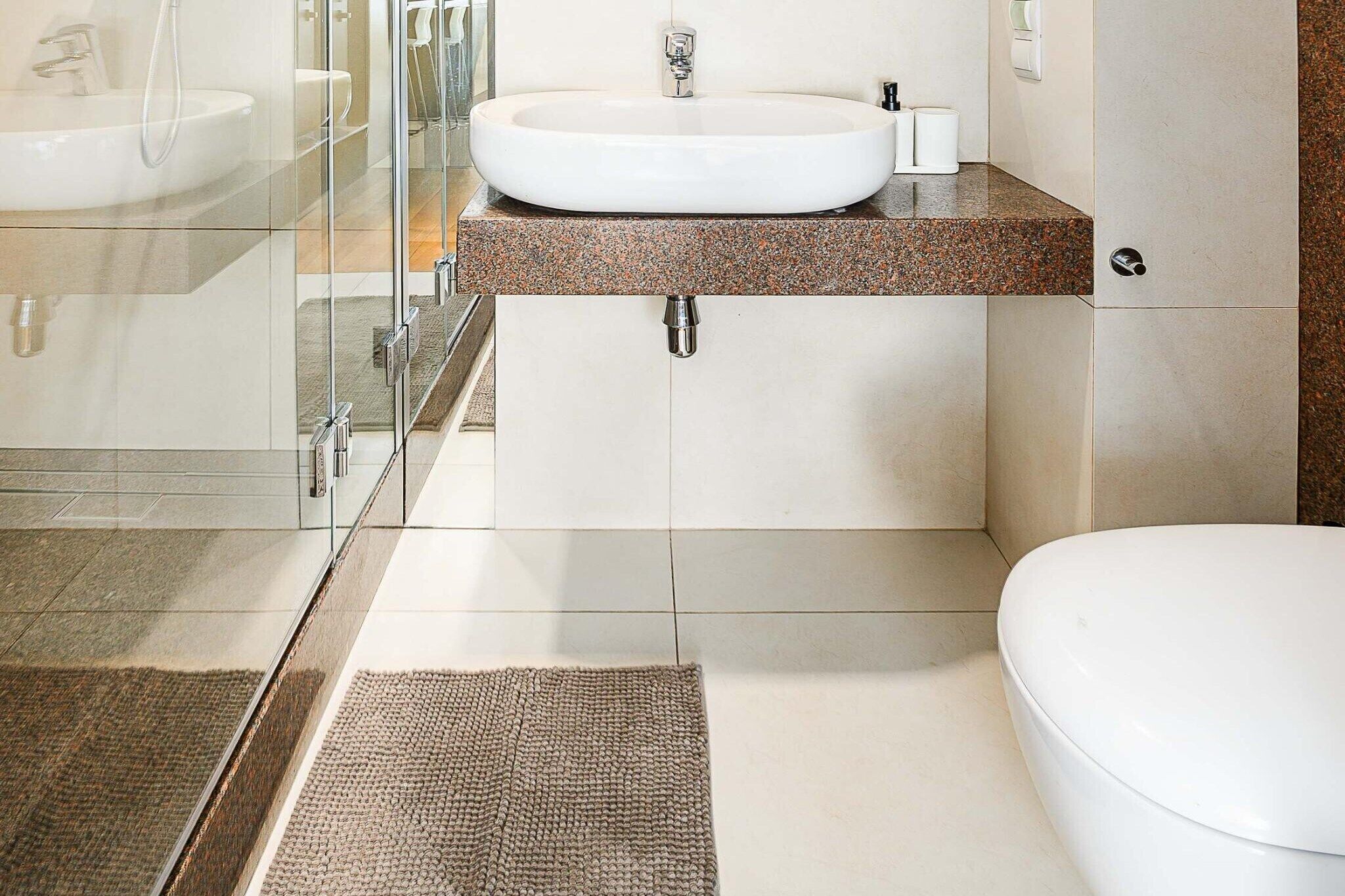 Un baño moderno con cabina de ducha de vidrio, un lavamanos blanco y un inodoro.