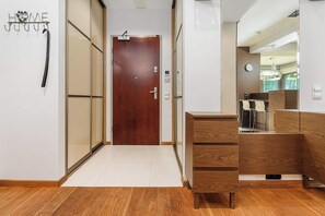 A hallway with a wooden door, a coat rack with hooks, and a wooden cabinet with drawers. - Parkside Flat with Private Garage (Łódź)