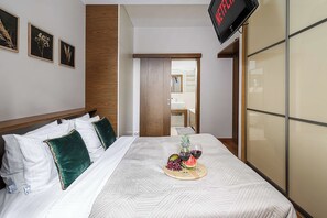 A hotel room with a bed, a TV, a wooden wardrobe, and a bathroom visible through an open door. - Parkside Flat with Private Garage (Łódź)
