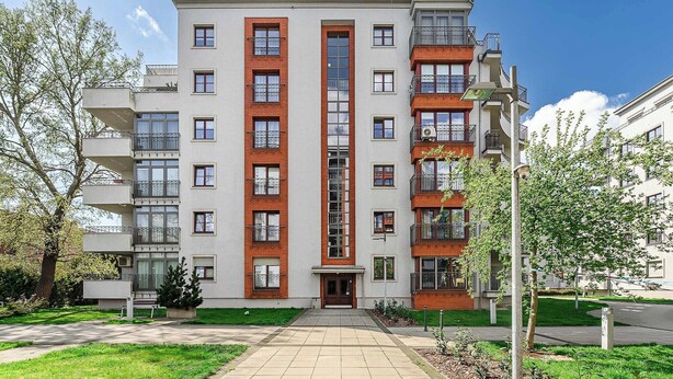 A multi-story residential building with a central entrance, balconies, and a surrounding green area. - Parkside Flat with Private Garage (Łódź)