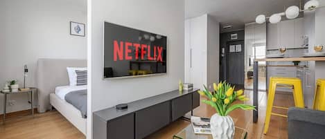 Una sala de estar moderna con un televisor de pantalla plana montado en la pared, un sofá, una mesa de centro y un área de cocina visible al fondo.