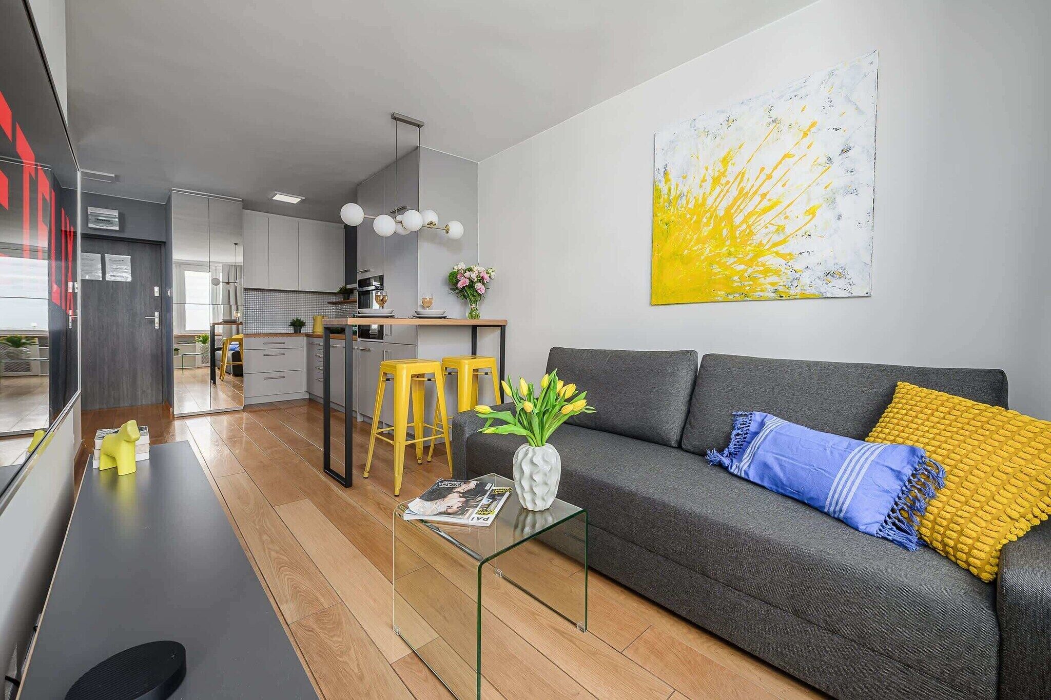 A modern living space with a grey sofa, yellow stools, and a glass coffee table.