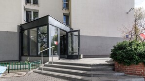 A building entrance with a glass door, steps leading up to it, and a small green fence. - Riverside Flat near Center (Warszawa)