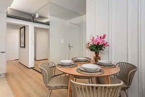 Een eetgedeelte met een ronde tafel voor vier personen, omringd door rieten stoelen, en een vaas met bloemen op de tafel.