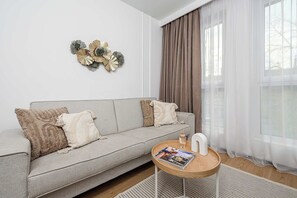 A modern living room with a grey sofa, decorative wall art, a round wooden coffee table, and sheer curtains. - Coastal Retreat for 4 with Terrace (Łódź)