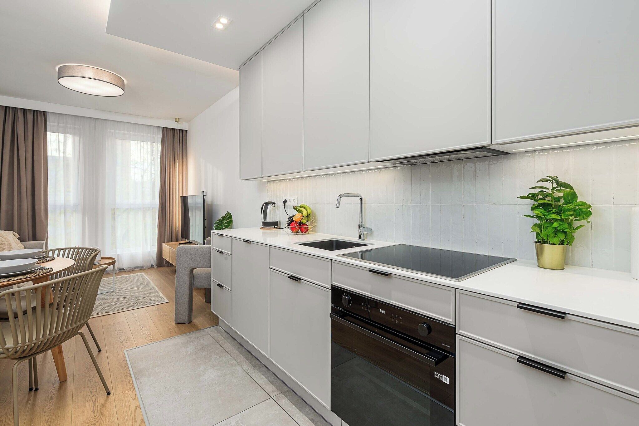 Een moderne keuken met witte kastjes, een zwarte spoelbak en een ingebouwde oven.