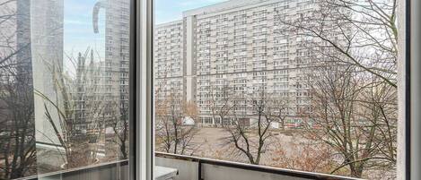 A high-rise residential building with multiple balconies, a clear sky, and leafless trees.