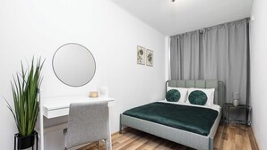 Quarto com cama, escrivaninha, cadeira, espelho, planta e mesa de cabeceira.