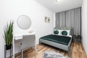 Ein Schlafzimmer mit Bett, Schreibtisch, Stuhl, Spiegel, Pflanze und Nachttisch.