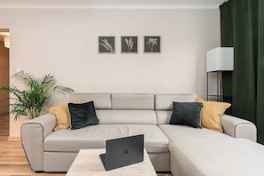 Ein modernes Wohnzimmer mit einem grauen Ecksofa, einem Couchtisch mit einem Laptop und einer Topfpflanze.