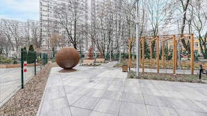 Uma passarela pavimentada com uma grande escultura esférica, bancos e um parquinho.