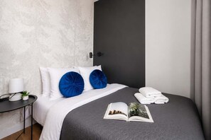 Una cama bien hecha con un edredón gris, dos almohadas azules y un libro sobre la cama.