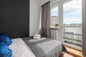 Une chambre d’hôtel avec un lit, une fenêtre avec des rideaux, un radiateur et une vue sur un immeuble et le ciel.