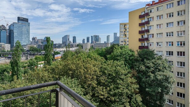 Un paisaje urbano con edificios modernos, cielo despejado y un balcón que da a un área verde.
