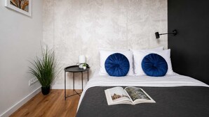 Un dormitorio con cama, dos almohadas azules, una mesita de noche con una planta y una lámpara de pared.