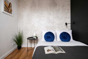 Ein Schlafzimmer mit einem Bett, zwei blauen Kissen, einem Nachttisch mit einer Pflanze und einer Wandlampe.