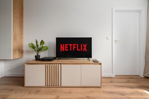 A modern living room with a wooden entertainment unit, a potted plant, a television displaying the Netflix logo, and a door in the background. - Flat near Warszawa Centralna (Warszawa)