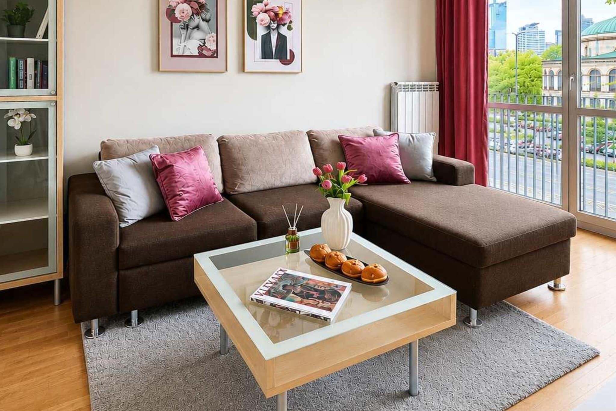Ein stilvolles Wohnzimmer mit einem braunen Sofa, einem Glastisch und Blick auf die Stadt durch große Fenster.