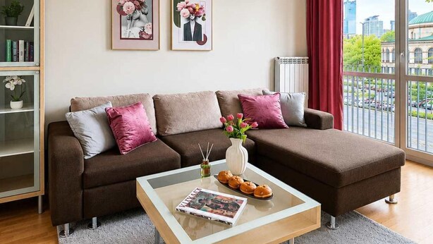 A modern living room with a brown sofa, a glass coffee table, and a view of the city through large windows. - Historic City Stay for 4 in Warsaw (Warszawa)