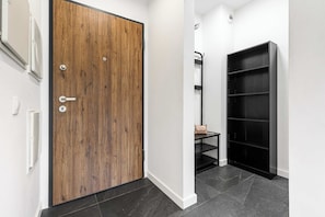 A hallway with a wooden door, a black shelving unit, and a small table with a bag. - Home near Historic District (Łódź)