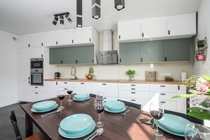 A modern kitchen with white cabinets, a central island with blue plates and wine glasses, and a built-in oven. - Home near Historic District (Łódź)