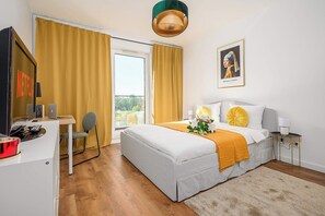 A hotel room with a bed, a desk with a computer, a chair, a window with curtains, and a painting on the wall. - Home near Historic District (Łódź)