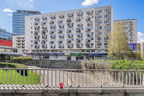 Un immeuble résidentiel à plusieurs étages, doté de balcons, d’un mur en pierre et d’une zone pavée agrémentée de bornes.