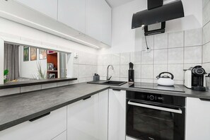 A modern kitchen with white cabinetry, a black countertop, a built-in oven, and a kettle. - Deluxe 4-Guest Apartment in Warsaw (Warszawa)