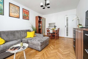 A living room with a grey sofa, a dining table with chairs, a bookshelf, and a television on a cabinet. - Deluxe 4-Guest Apartment in Warsaw (Warszawa)