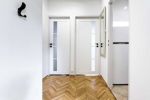A hallway with two white doors, one with a frosted glass panel, and a wooden herringbone floor. - Deluxe 4-Guest Apartment in Warsaw (Warszawa)