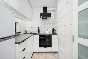 A modern kitchen with white cabinetry, a black range hood, and a built-in oven. - Deluxe 4-Guest Apartment in Warsaw (Warszawa)