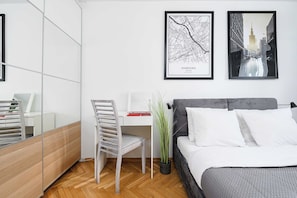A modern bedroom with a bed, a desk, and a chair. There are two framed pictures on the wall.