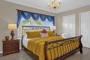 A bedroom with a bed, two bedside tables, a chandelier, and a window with blue curtains. - 7-bedroom Villa POOL, HOT TUB & GAME ROOM! (Kissimmee)