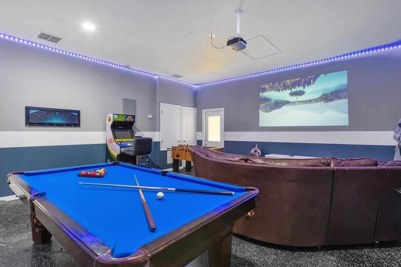 Een pooltafel met ballen, een tafelvoetbalspel en een projectiescherm waarop een besneeerd landschap te zien is.