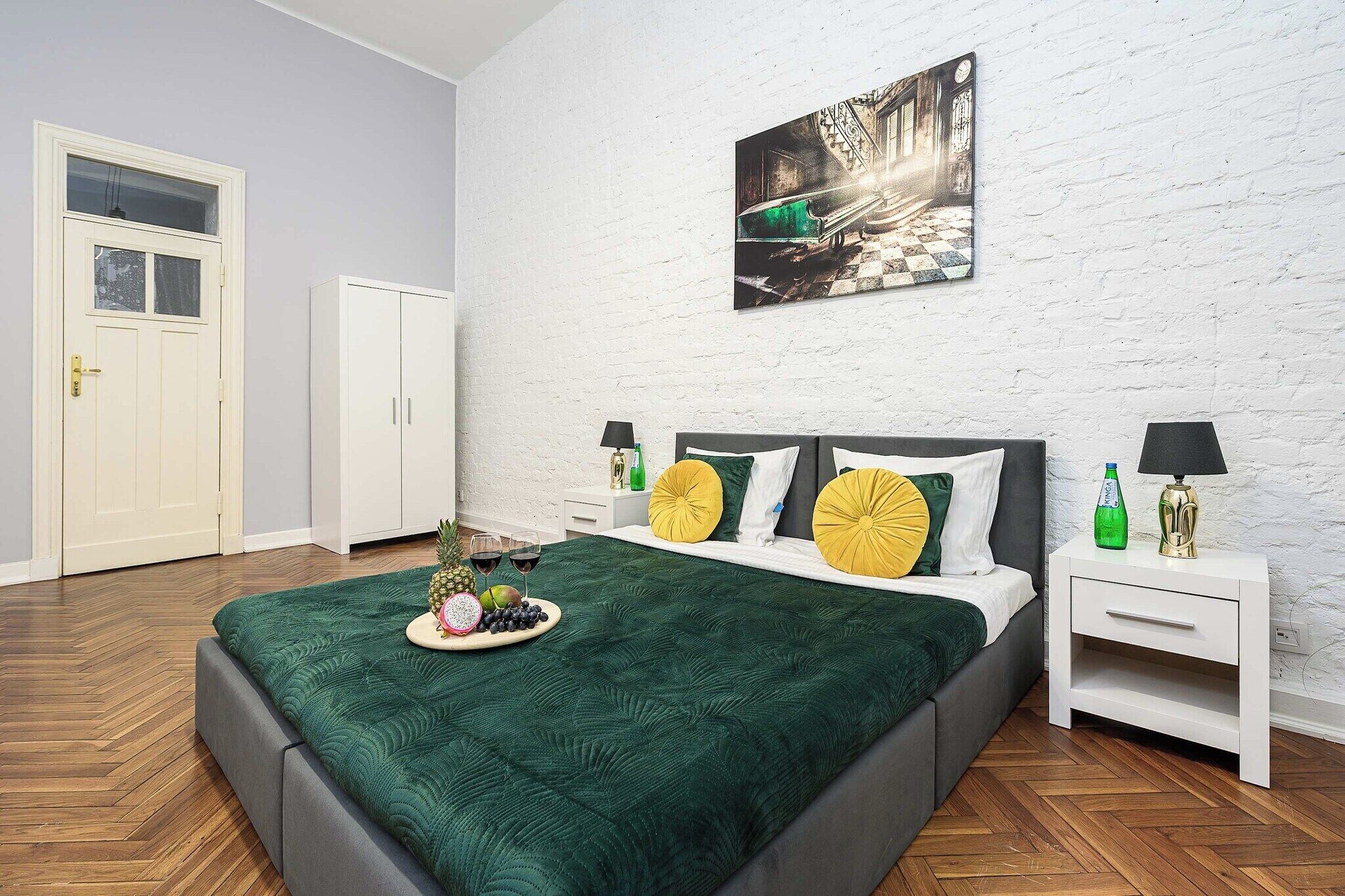 A bedroom with a bed, a nightstand, a wardrobe, a door, and a wall-mounted picture.